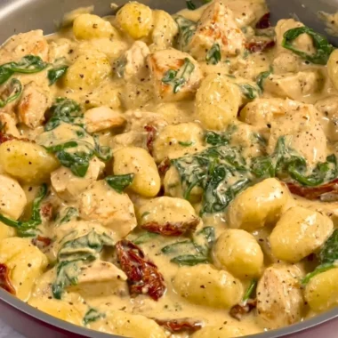 Bowl of creamy chicken gnocchi with herbs and spices on a wooden table