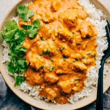Delicious crockpot butter chicken served with rice and garnished with cilantro