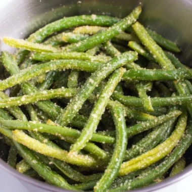 A plate of crispy air fryer parmesan green beans garnished with herbs.