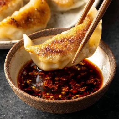 Homemade dumpling dipping sauce in a small bowl with dumplings on the side