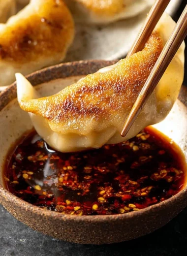 Homemade dumpling dipping sauce in a small bowl with dumplings on the side